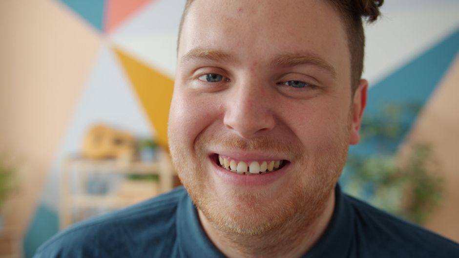 Retrato de un hombre sonriente en interiores con un fondo geométrico colorido.
