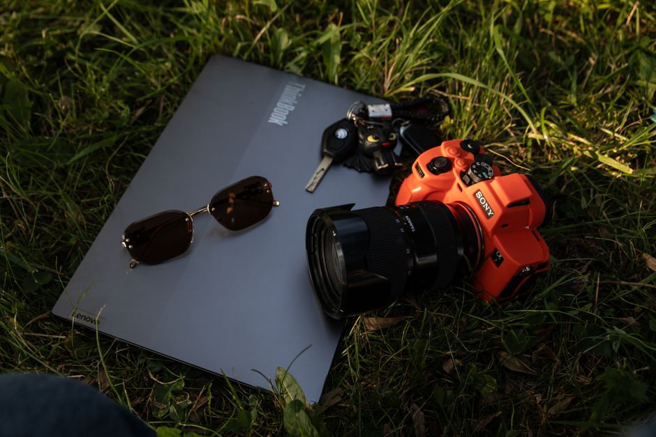Una cámara, un ordenador portátil y unas gafas de sol reposan sobre la hierba, la imagen por excelencia de la fotografía al aire libre.