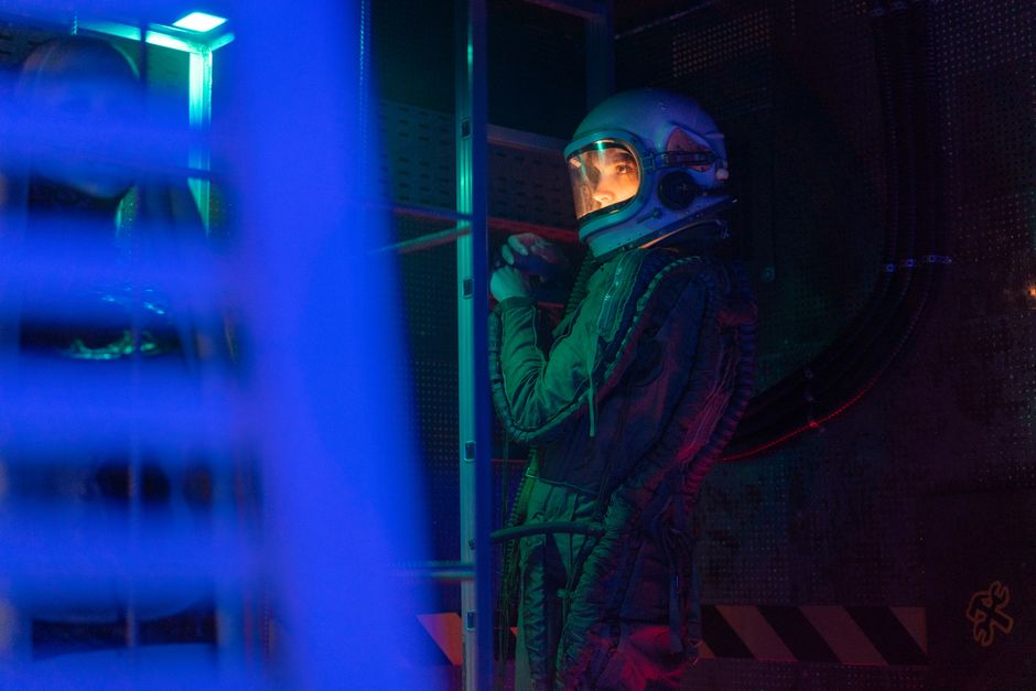 Una astronauta femenina en un traje espacial se encuentra en un transbordador espacial iluminado con luces de neón, lista para la exploración interestelar.
