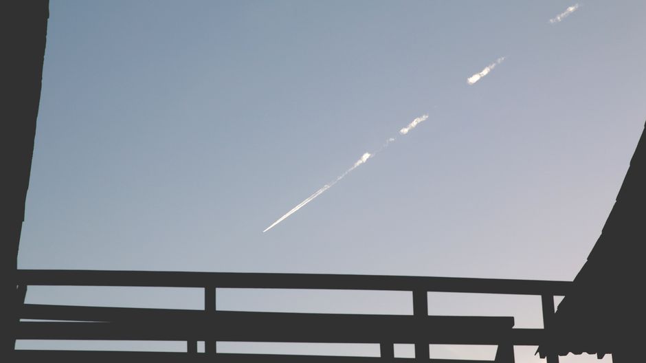 Silueta de una estructura con un rastro de avión en el cielo azul claro contrastando con ella.