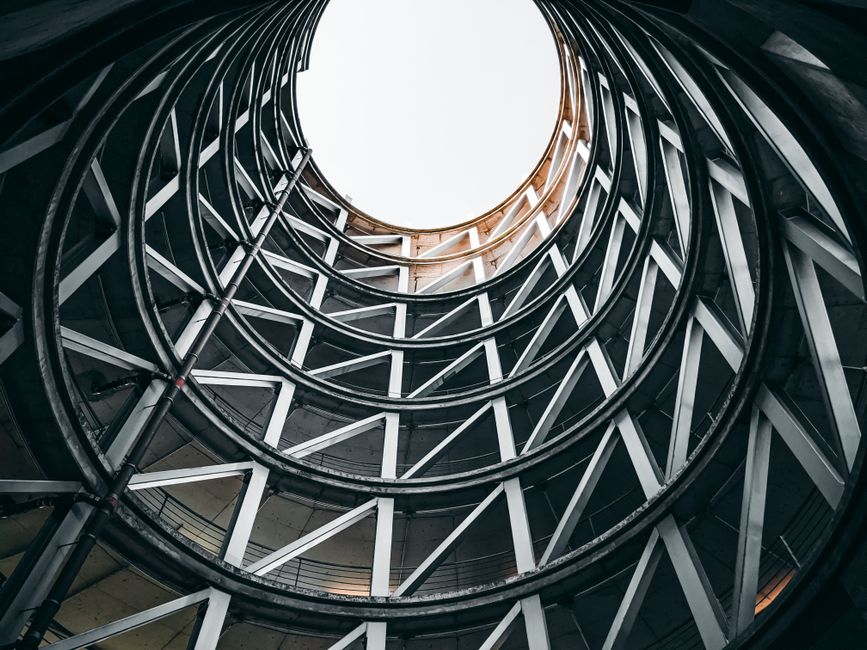 Vista en plano bajo del interior de un moderno aparcamiento en espiral con diseño geométrico y cielo abierto brillante.