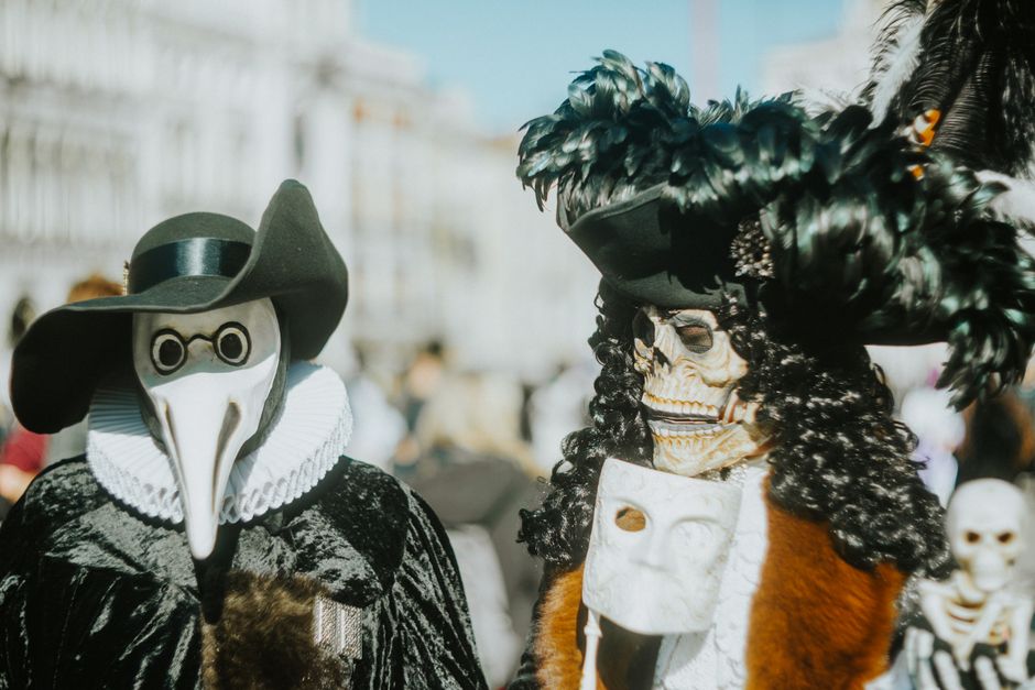 Dos personas con elaboradas máscaras venecianas en un festivo desfile de carnaval, capturando un encanto histórico y misterioso.