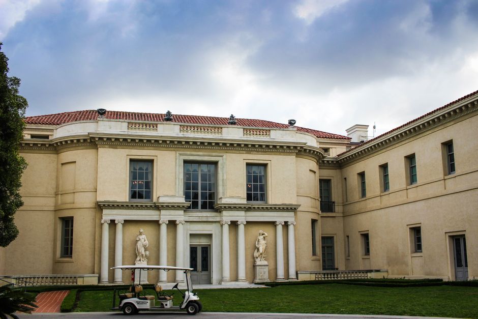 Elegante edificio neoclásico con grandes columnas, estatuas y un carro de golf sobre césped exuberante.