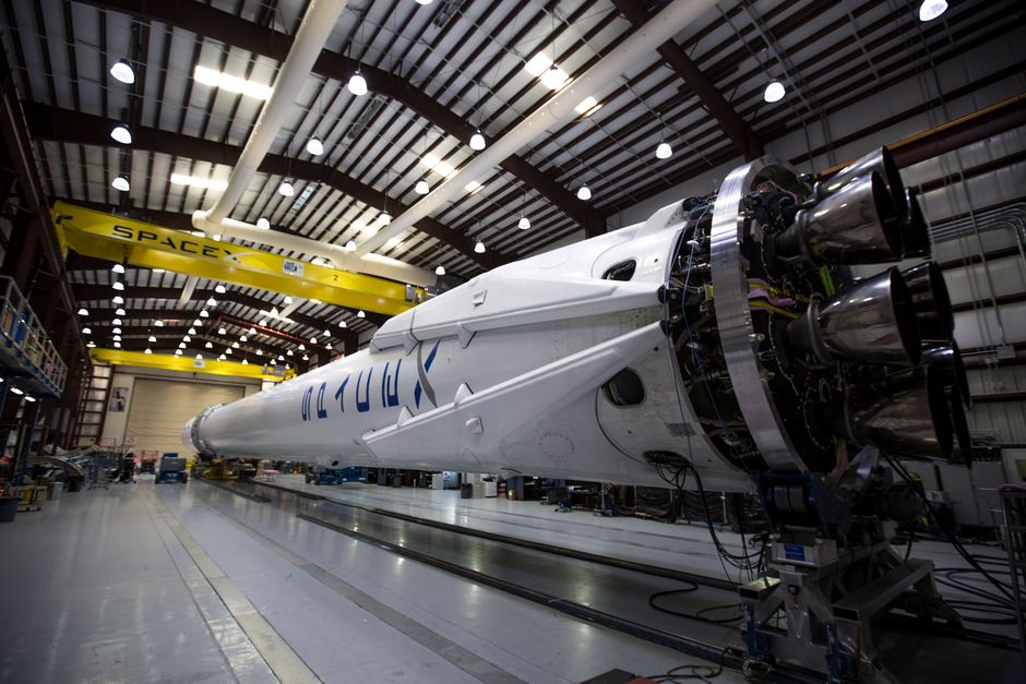 Un cohete Falcon de SpaceX exhibido en un hangar amplio bajo luces industriales brillantes.