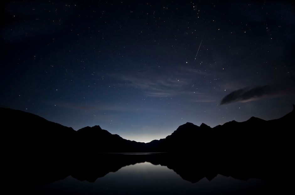 Un impresionante cielo estrellado con siluetas de montañas y reflejos en el lago en Montana.