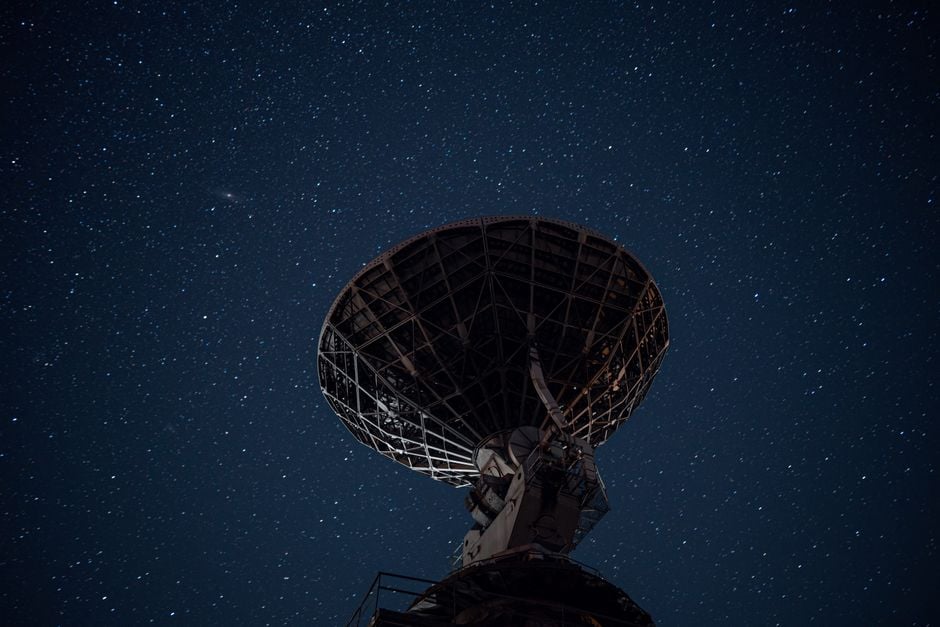 Silueta de una antena parabólica contra un cielo nocturno estrellado, capturando la exploración cósmica.