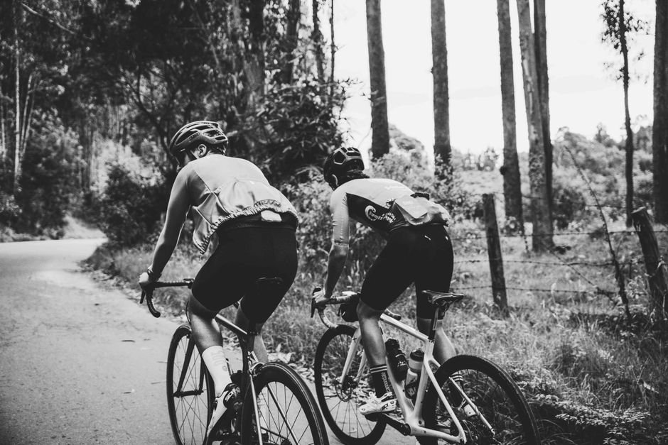 Dos ciclistas en bicicletas de ruta recorren una carretera entre árboles.