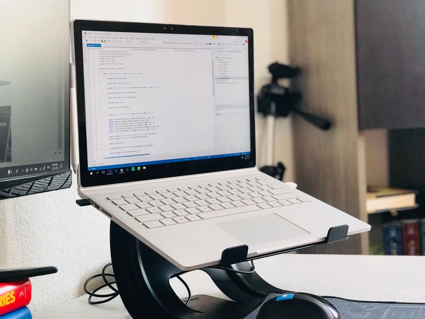 Un setup de oficina en casa con un laptop en un soporte y un monitor, ideal para el trabajo remoto.