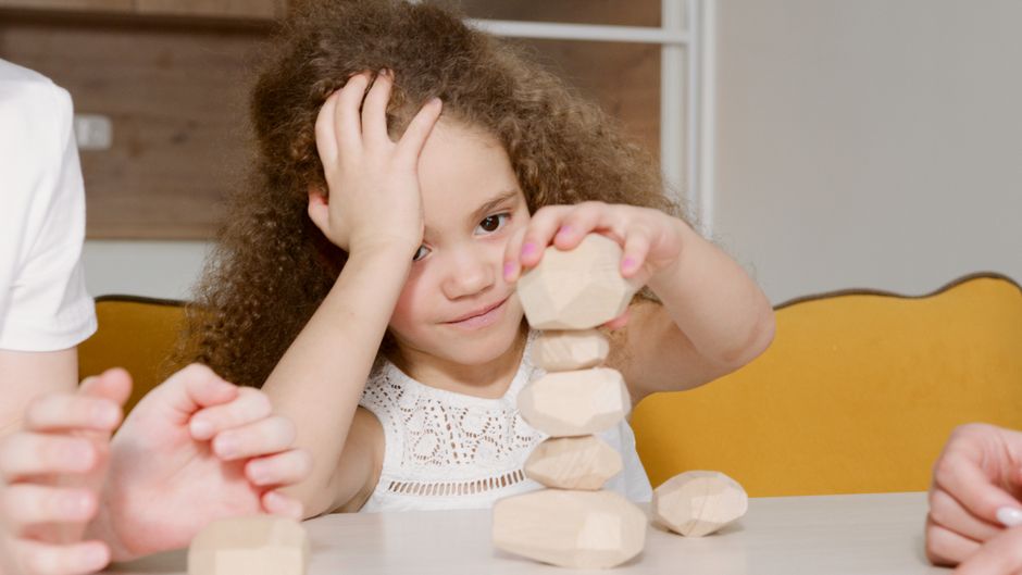 Una niña pequeña juega con bloques de madera, apilándolos cuidadosamente en un ambiente acogedor en el interior.
