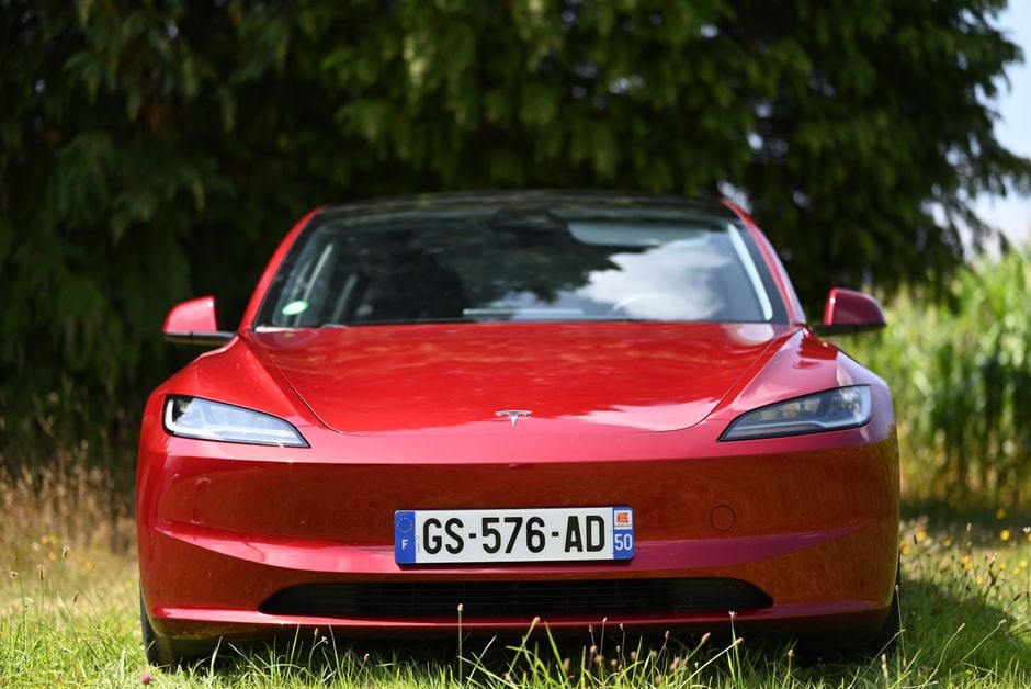 Un llamativo coche eléctrico rojo estacionado al aire libre con árboles verdes exuberantes de fondo.