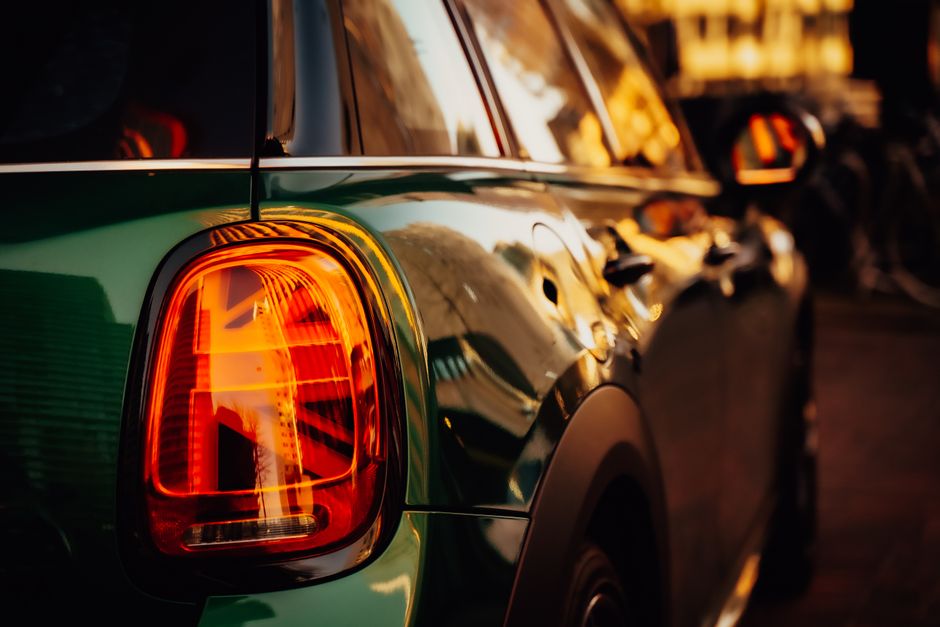 Foto detallada del piloto trasero de un coche verde brillante reflejando el resplandor del atardecer. Ideal para temas automotrices.