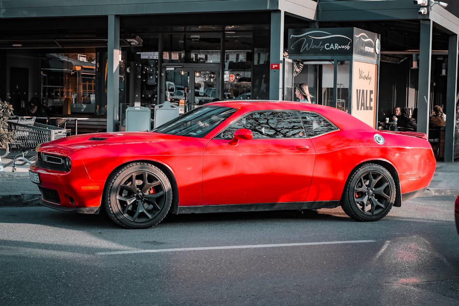 Un automóvil deportivo de color rojo brillante estacionado afuera de un lavadero de autos urbano, resaltando su elegante diseño.