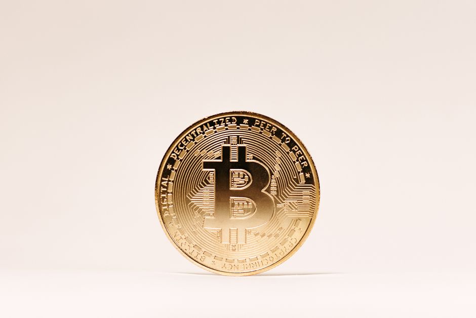 Una moneda de Bitcoin dorada de pie sobre un fondo claro minimalista.