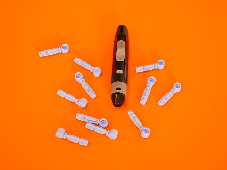 Vista superior de un glucometro y lancetas sobre un fondo naranja brillante para el manejo de la diabetes.