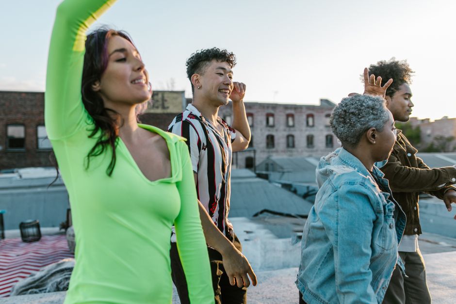Un grupo animado de amigos diversos disfrutando de un baile en una azotea de la ciudad al atardecer.