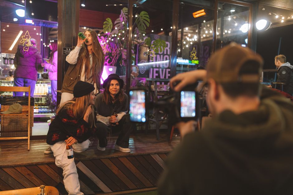 Grupo de amigos disfrutando de la vida nocturna, usando ropa de calle moderna, capturados de manera candid en frente de un bar.