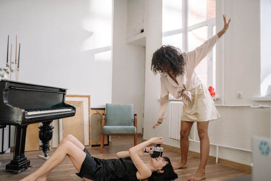 Dos mujeres en una divertida sesión de fotos en interiores con un piano, capturando momentos creativos juntas.