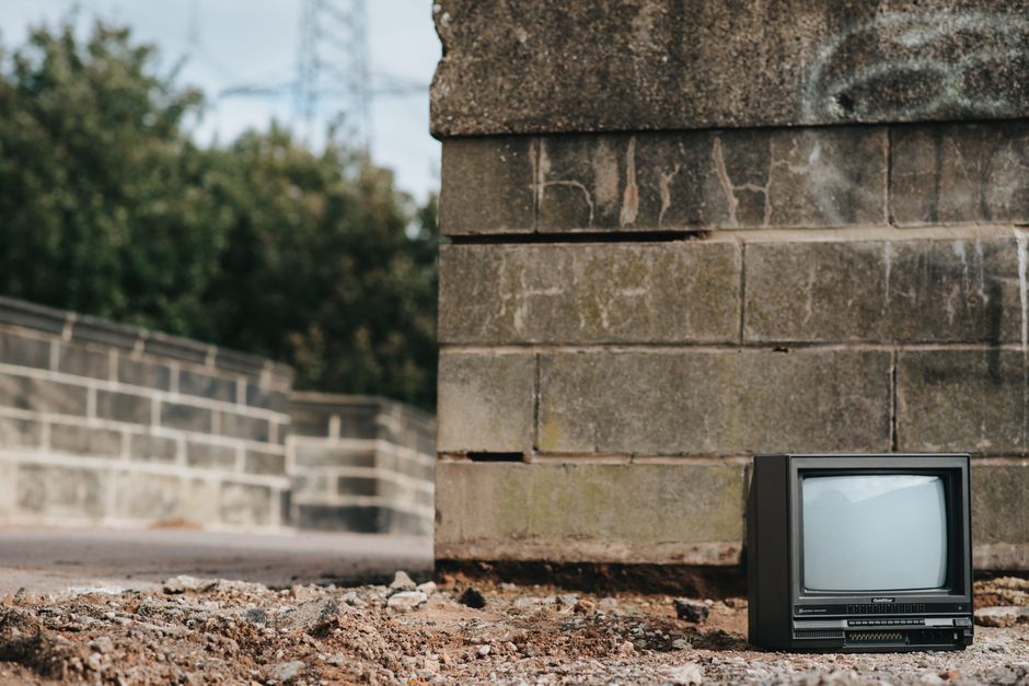 Un viejo televisor colocado junto a una pared de cemento desgastada en un área urbana abandonada con un fondo de ciudad desenfocado.