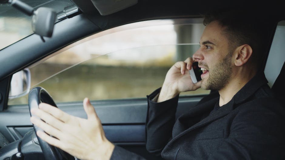 Hombre en el coche hablando por teléfono móvil mientras conduce, mostrando frustración.