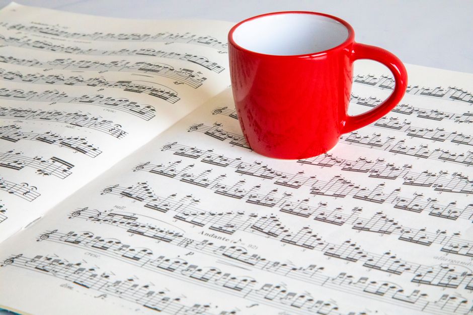 Una vibrante taza roja colocada sobre una partitura abierta, creando una composición de naturaleza muerta armoniosa.