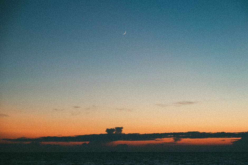 Un cielo crepuscular tranquilo con una luna creciente sobre un océano sereno, capturando la belleza serena de la naturaleza.