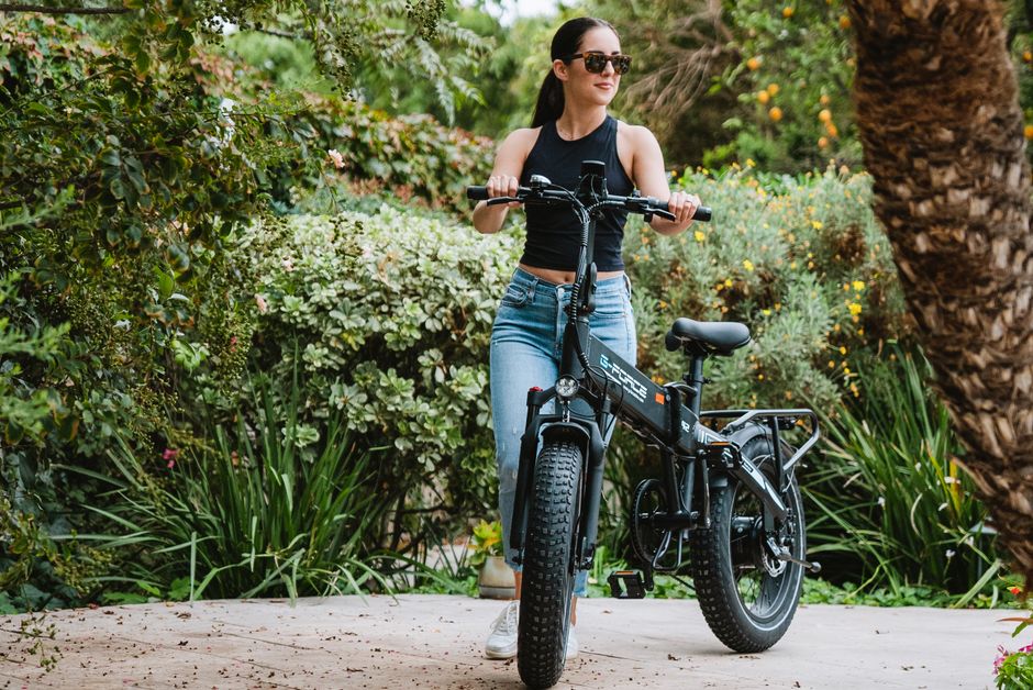 Joven disfrutando de un paseo en una bicicleta eléctrica, rodeada de exuberante vegetación verde, en un día soleado.