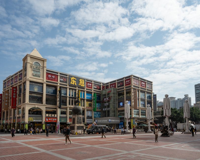 Plaza animada de la ciudad de Guangzhou con gente, tiendas y cielo azul.