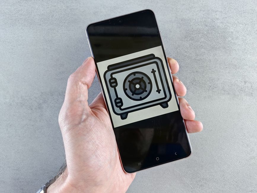 Close-up de un smartphone mostrando un ícono de caja fuerte sostenido en una mano, simbolizando la seguridad digital.