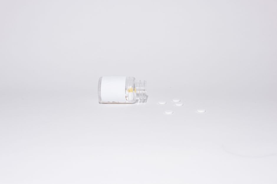 Foto minimalista de pastillas blancas y una botella abierta sobre un fondo blanco, enfatizando la vacuidad.