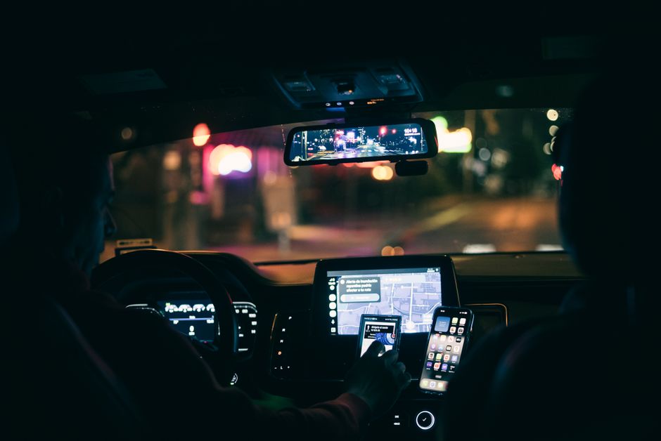 Vista interior de un coche por la noche, con un conductor utilizando un smartphone para la navegación por las calles de la ciudad.