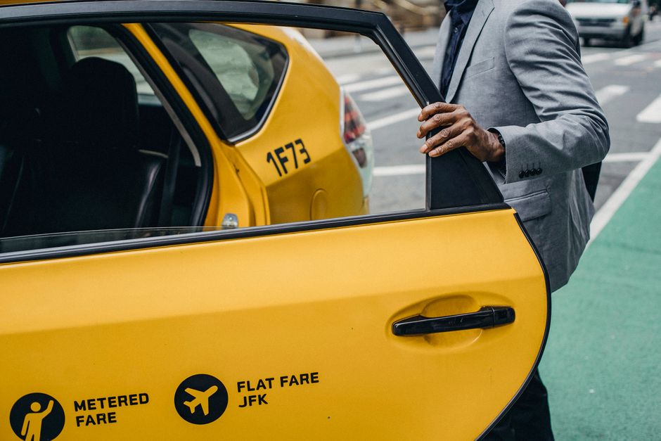 Empresario con traje subiendo a un taxi amarillo en una calle de la ciudad, mostrando el transporte y la movilidad urbana.