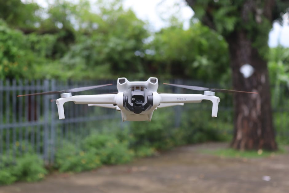 Dron blanco flotando en un parque con follaje verde, mostrando tecnología moderna.