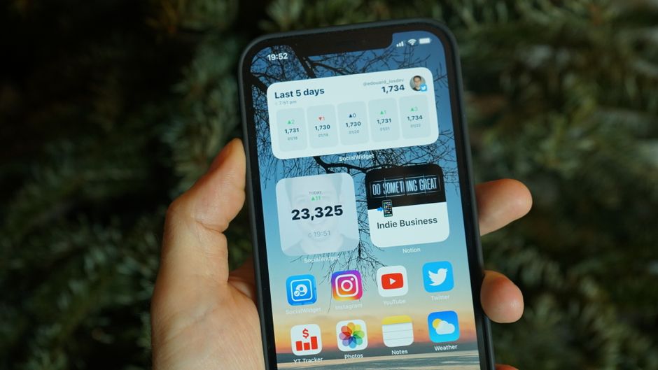 Una mano sosteniendo un smartphone que muestra varios widgets de la pantalla de inicio e íconos de aplicaciones.