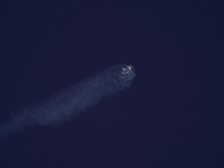 Un cuerpo celeste brillante atraviesa el oscuro cielo nocturno dejando una estela de humo.