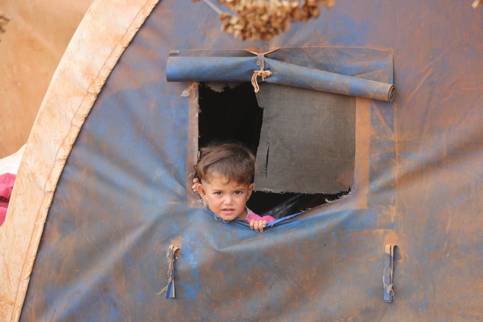 Un niño pequeño asoma por la ventana de una tienda, simbolizando resiliencia en Idlib, Siria.