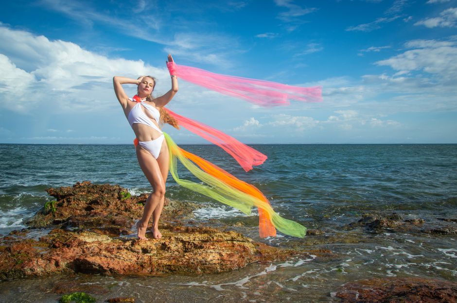 Mujer disfrutando de la playa en bikini con pañuelos coloridos, personificando la libertad y el ambiente veraniego.