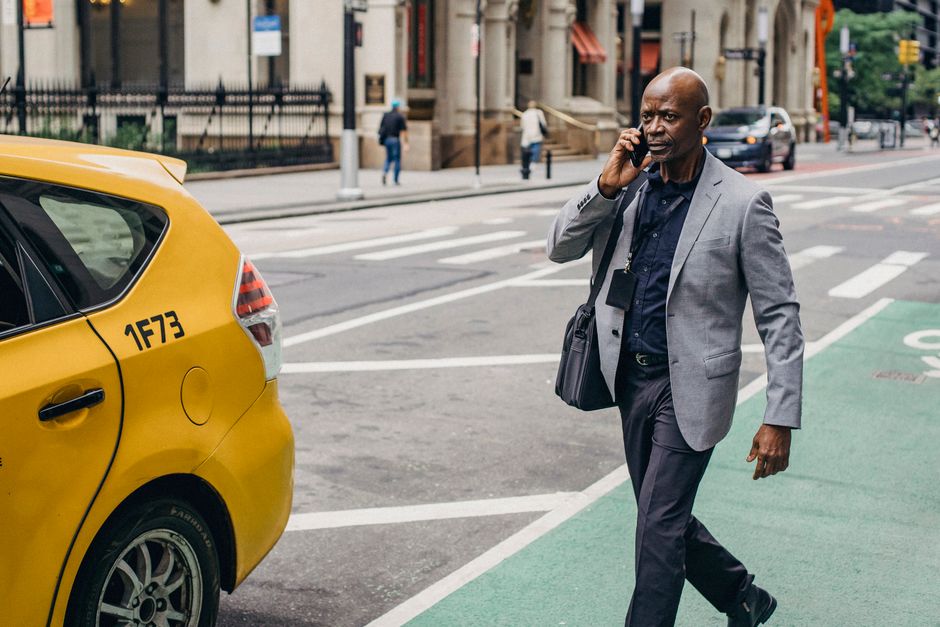 Un hombre bien vestido cruzando una calle de la ciudad mientras habla por su celular cerca de un taxi amarillo.