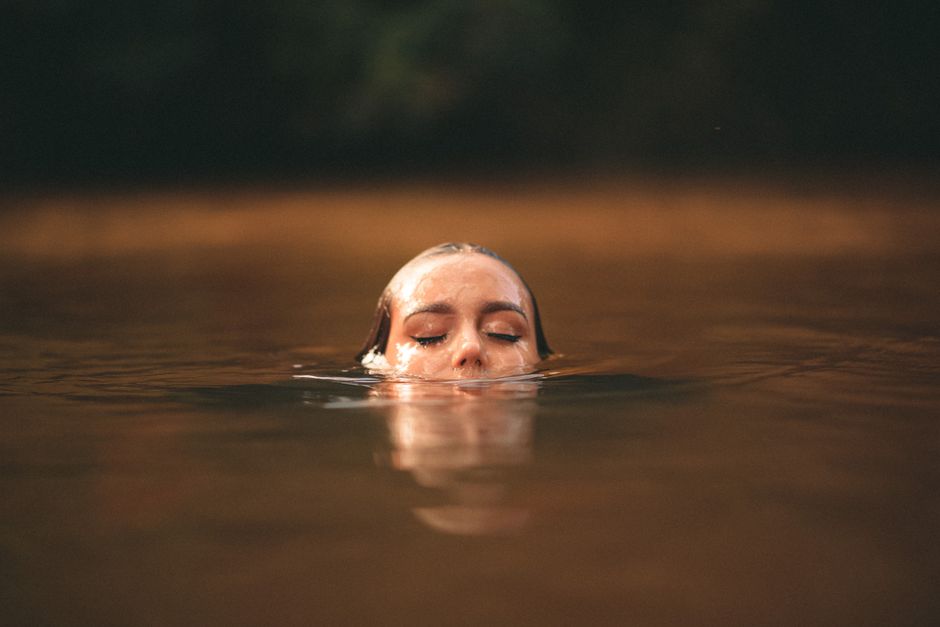 Una imagen serena de una joven nadando con los ojos cerrados en un lago pacífico.