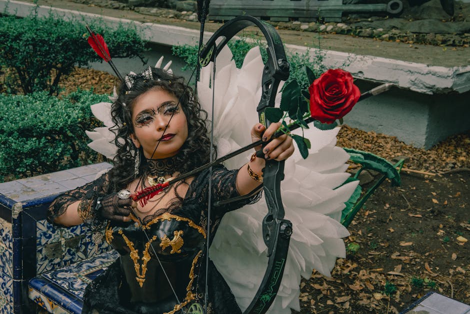 Mujer con alas de ángel en traje de carnaval mostrando un maquillaje intrincado y sosteniendo un arco con una flecha rosa.