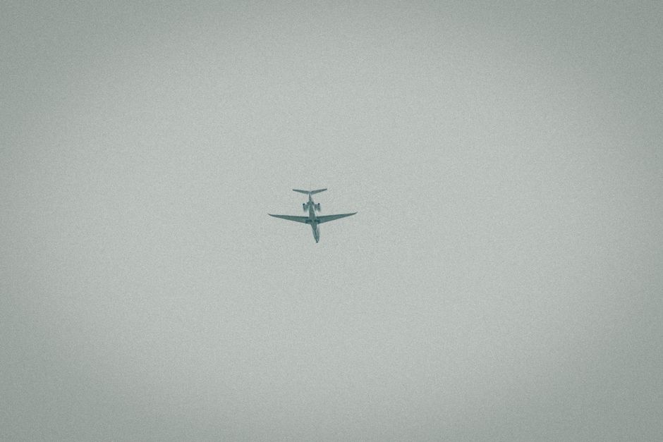Un avión solitario capturado en pleno vuelo contra un cielo nublado, simbolizando viaje y aventura.
