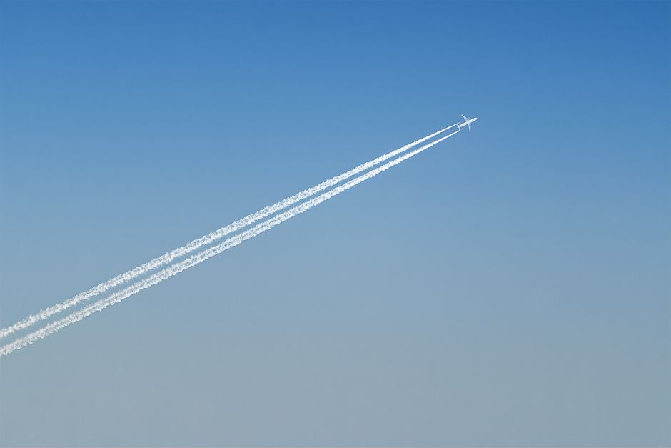Un avión creando estelas de nubes en un cielo azul claro, mostrando la tecnología de la aviación.