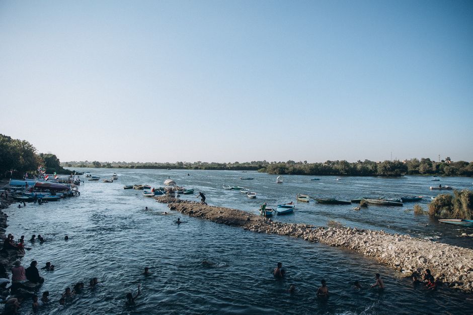 Personas nadando y barcos anclados en el Nilo en Al Qanatir, Egipto en un día soleado.