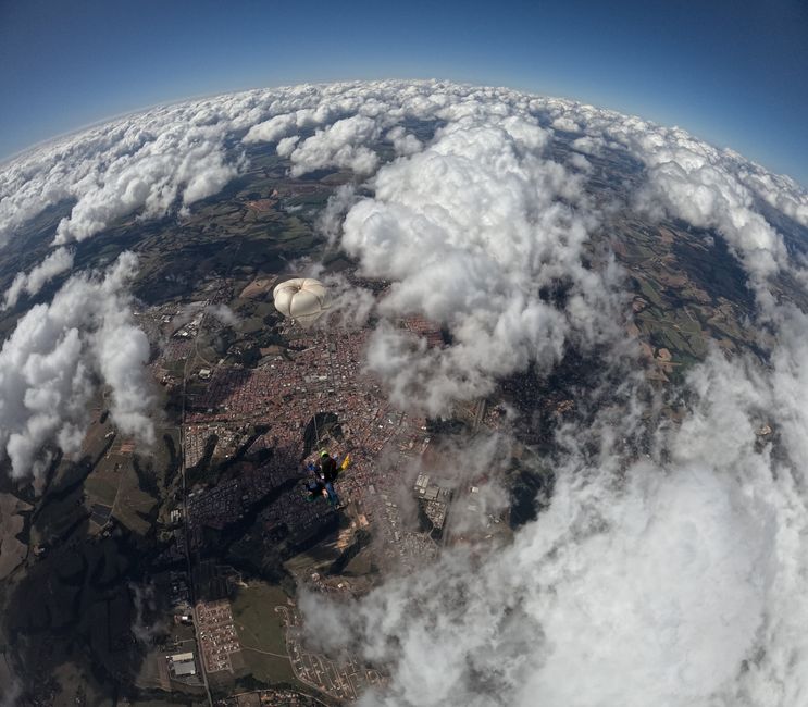 Paracaidista con paracaídas sobre la ciudad y nubes, perspectiva aérea.