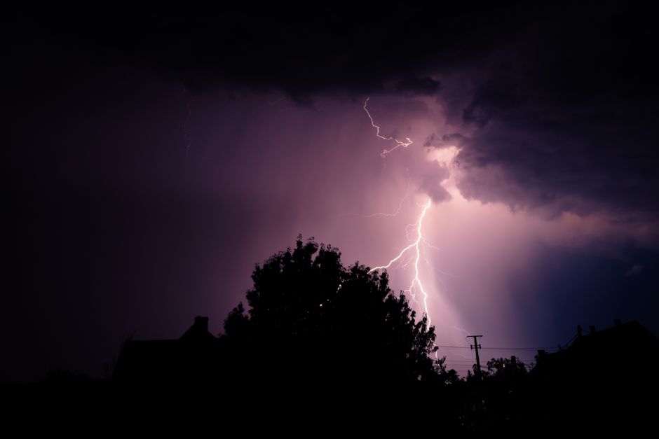 Silueta de árboles iluminados por un rayo durante una tormenta nocturna.