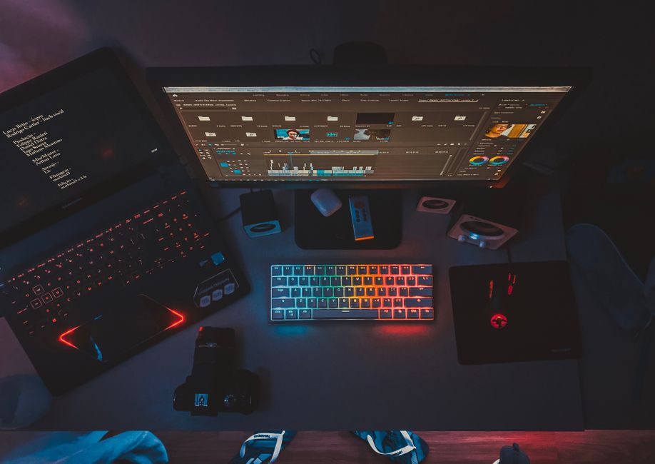 Un espacio de trabajo contemporáneo con monitores dobles, un teclado iluminado en arcoíris y software de edición, perfecto para entusiastas de la tecnología.
