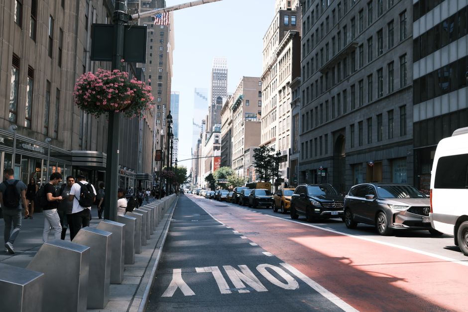 Una calle animada en Nueva York con gente, coches y altos edificios bajo un cielo despejado.