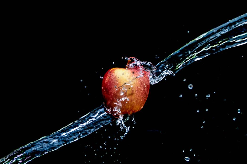 Primer plano de una manzana roja salpicando en agua sobre un fondo oscuro.