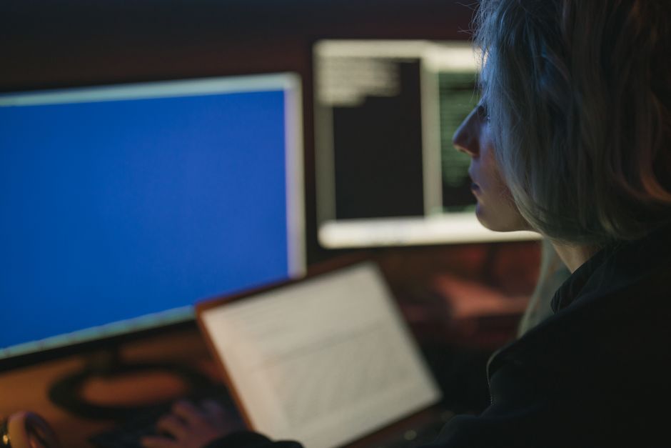 Una mujer trabajando en varias pantallas de computadora por la noche, enfocándose en sus tareas.