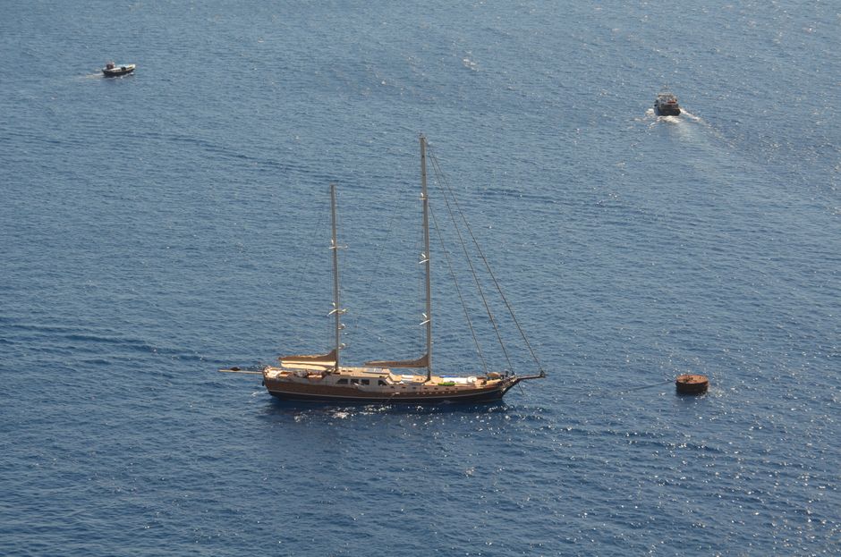 Vista aérea de un yate navegando en las aguas azules cerca de Fira, Grecia, mostrando la tranquilidad del verano.