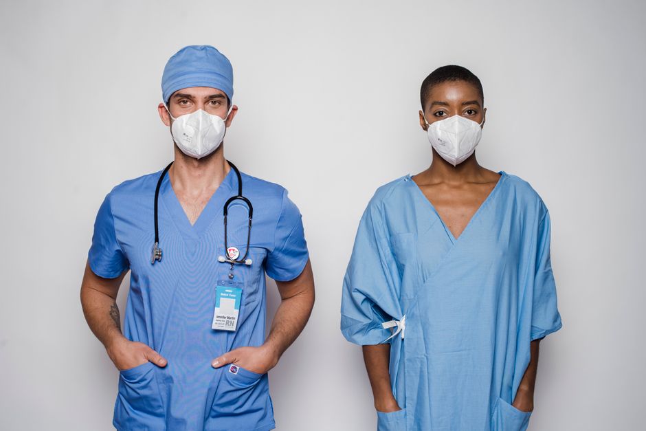 Dos profesionales de la salud en uniformes azules y mascarillas de pie juntos en un estudio.